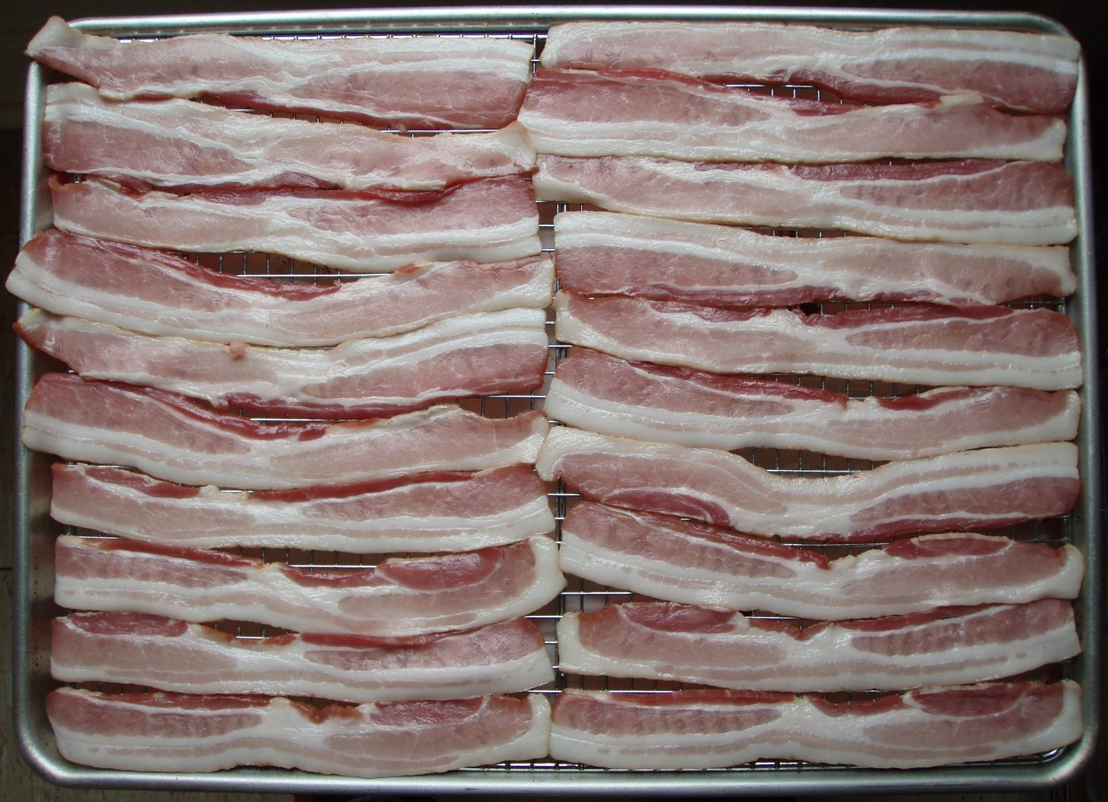 Raw streaky bacon rashers laid out on a metal rack