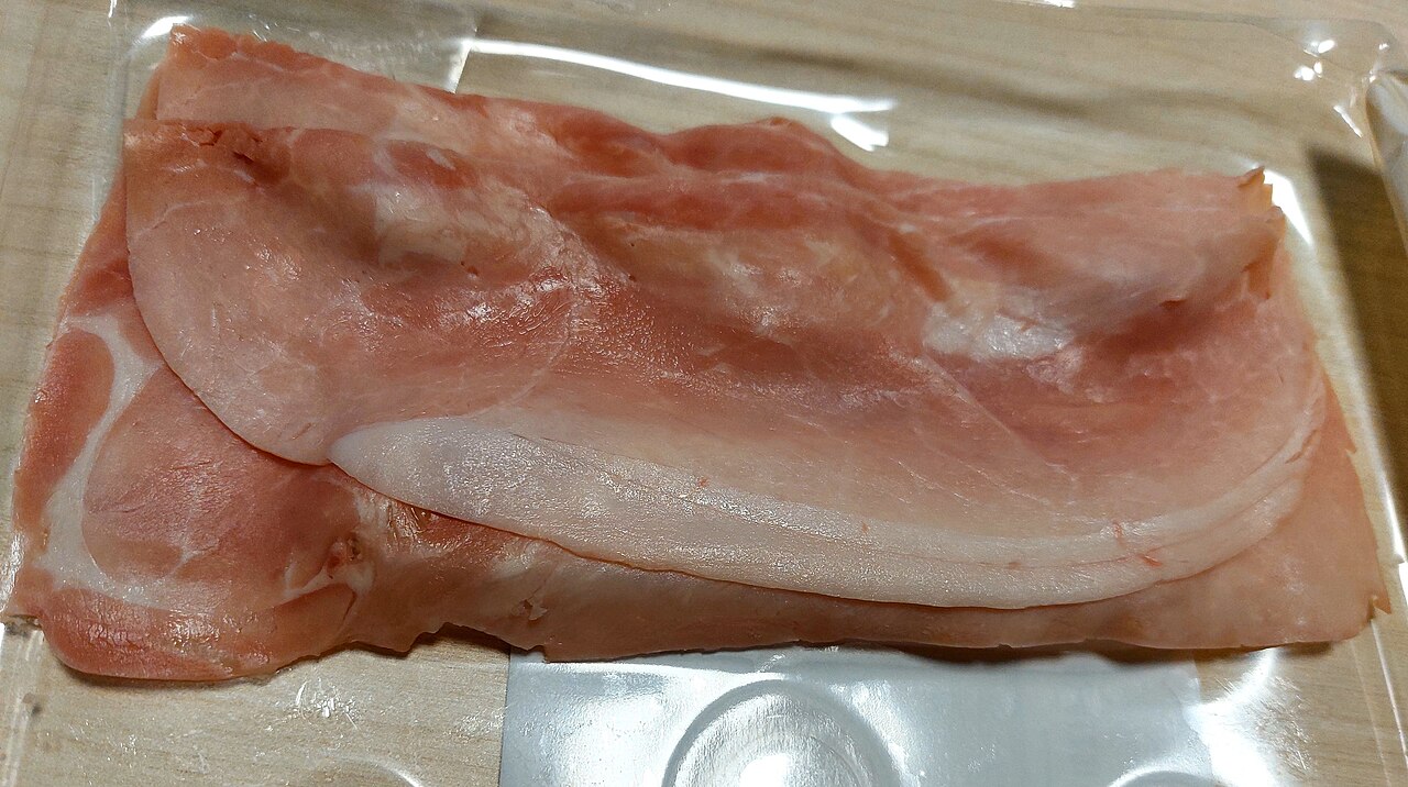 Slices of cooked pink ham fanned out on a board