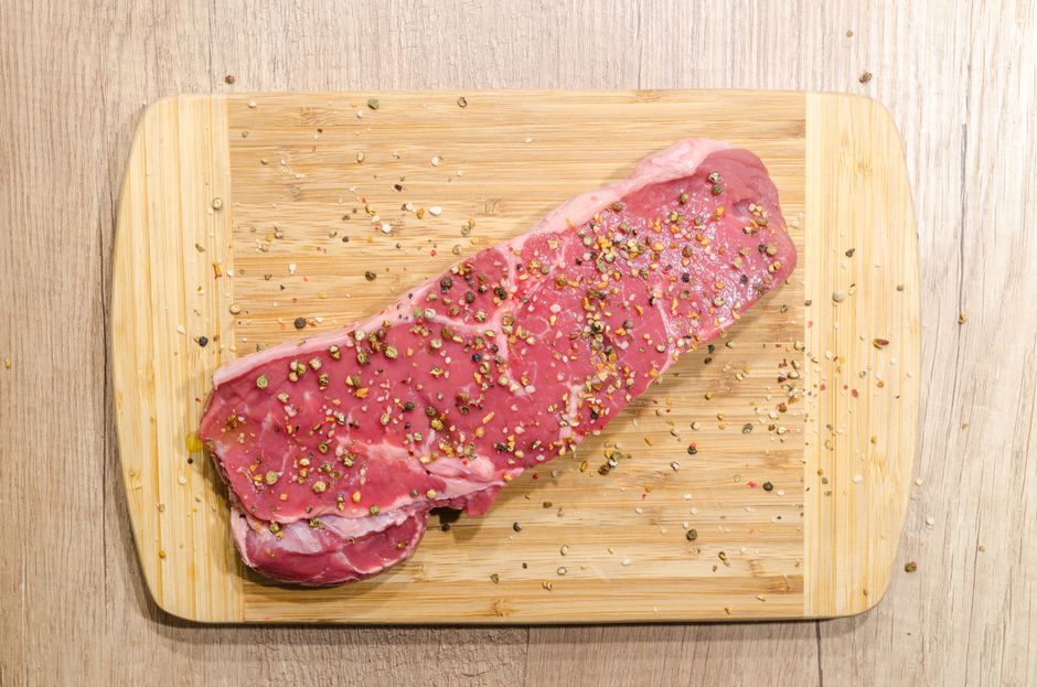 A raw beef steak seasoned on a wooden board